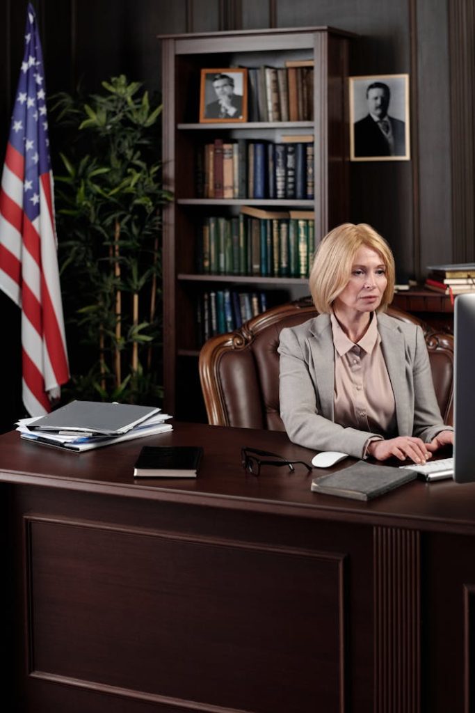 A businesswoman in a formal office with an American flag background, working at her desk.